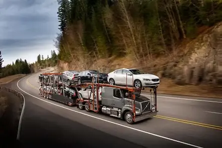 A car carrier truck transporting severals cars on a flatbed trailer traveling down a highway.