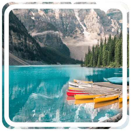 A group of canoes docked on a calm lake with lush green trees covering the mountains in the background.