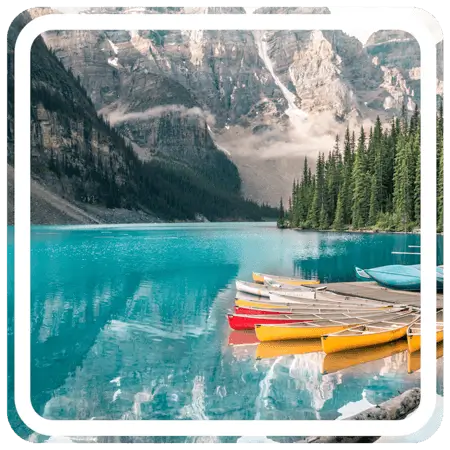 A group of canoes docked on a calm lake with lush green trees covering the mountains in the background.