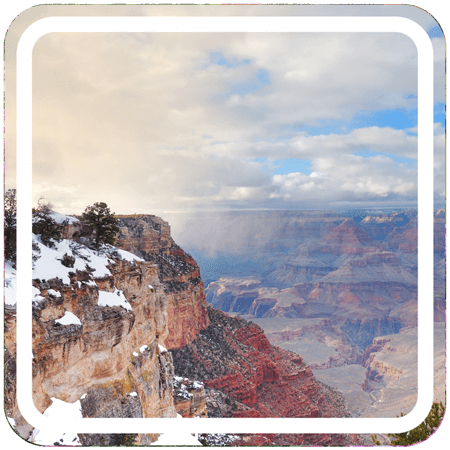 A wide view of the Grand Canyon from the South Rim. The canyon is vast and colorful, with layered bands of red, brown, and yellow rock. 