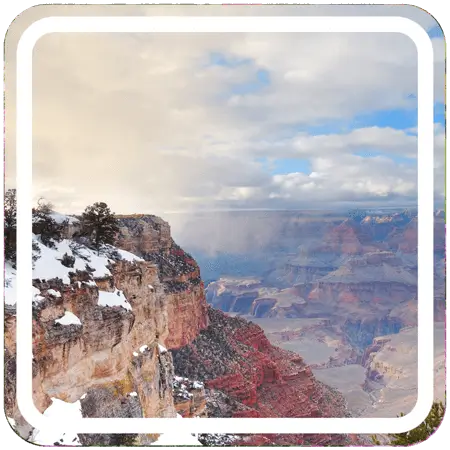 A wide view of the Grand Canyon from the South Rim. The canyon is vast and colorful, with layered bands of red, brown, and yellow rock. 