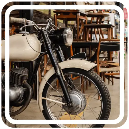 A black motorcycle with chrome detailing is parked on a sidewalk in front of a row of brown chairs.