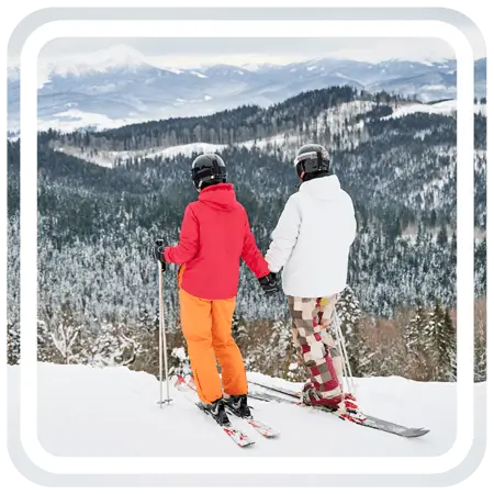 Two people holding each other's hands while skiing