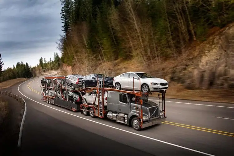 A car carrier truck transporting severals cars on a flatbed trailer traveling down a highway.