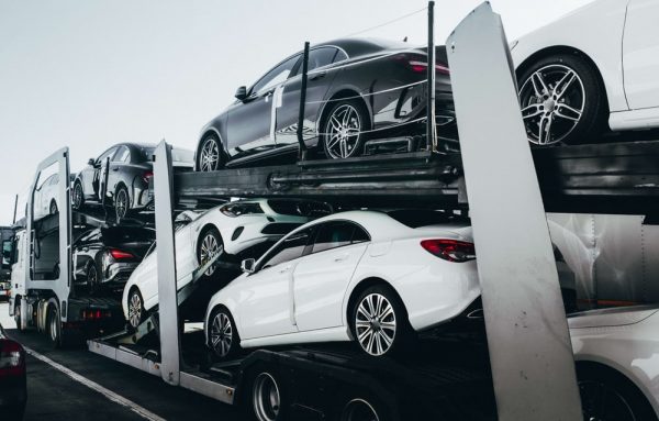 This image shows a silver car carrier truck transporting several cars 