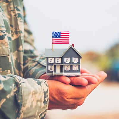 A military person holding a toy house with american flag on top of it