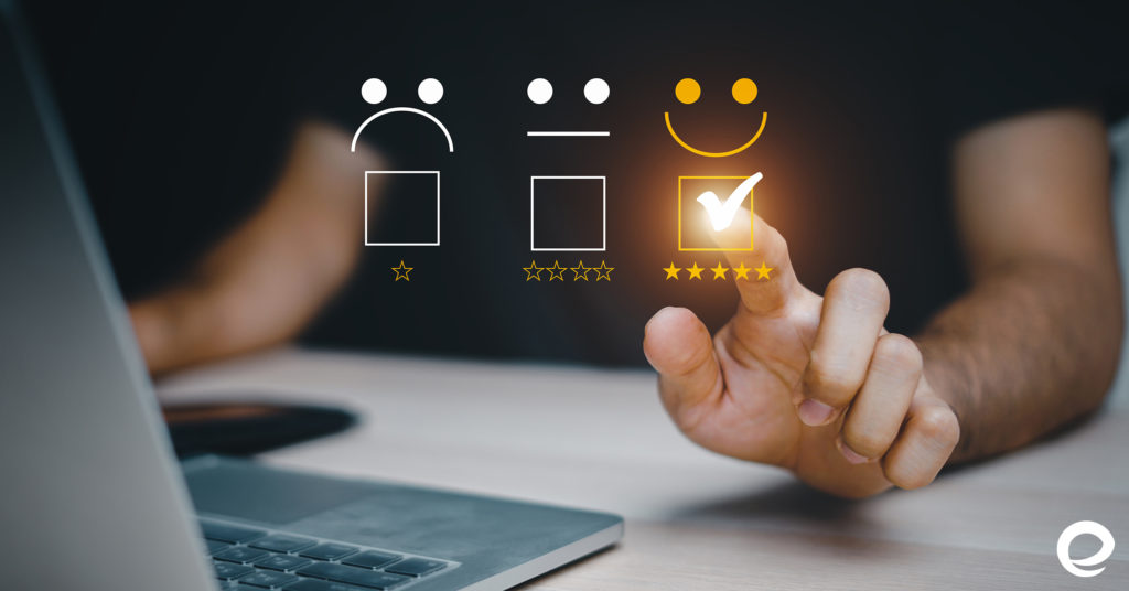 There are three emojis, sad, poker face, and happy face. Below them are ratings of one star, four stars, and five stars, respectively, for the happy face. In the background, a person is using a laptop and pointing at the happy face. This symbolizes customer satisfaction