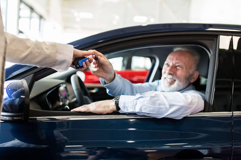 Happy old man inside car taking key of his car