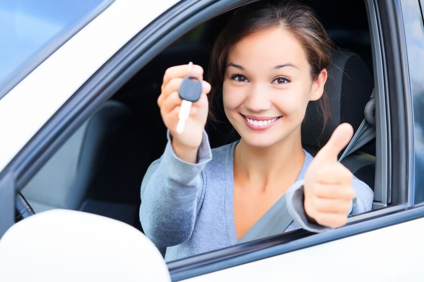 A  woman inside a car showing her key to the camera while giving a thumbs up