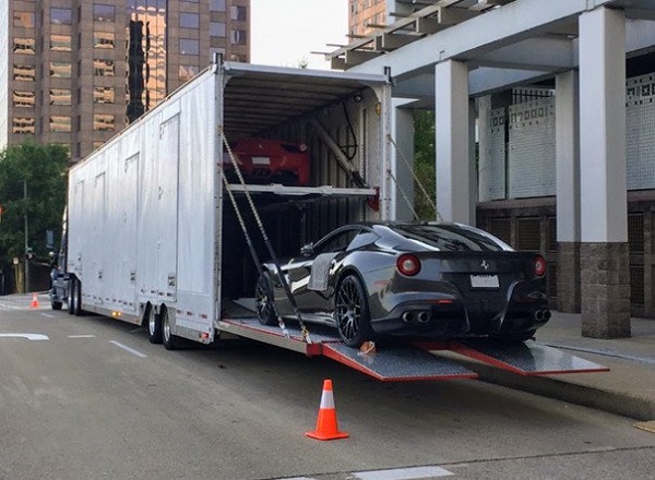 An enclosed car carrier being loaded with a sports car