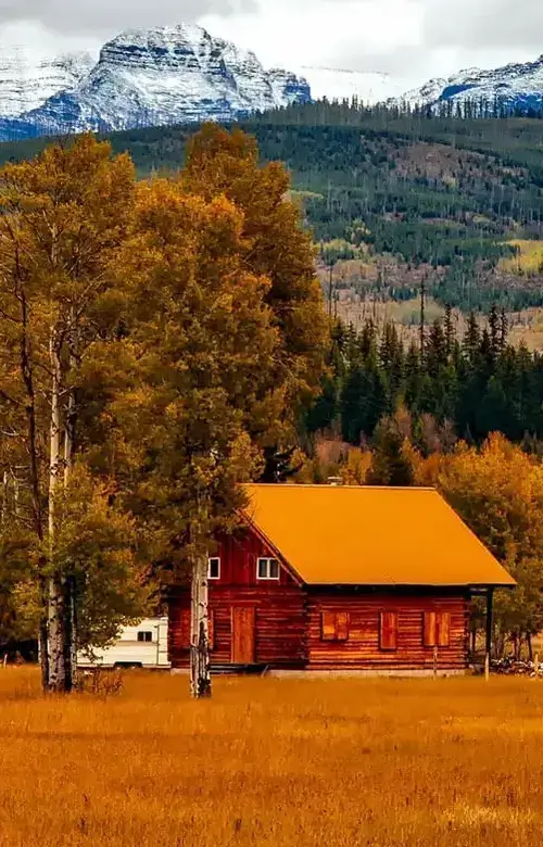 A log cabin nestled in a meadow, with the majestic peaks of the Rocky Mountains towering in the distance