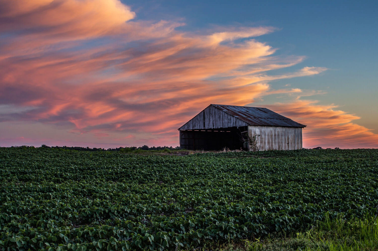 A peaceful Indiana farm scene at dusk, with a red barn and silo bathed in the warm glow of the setting sun.