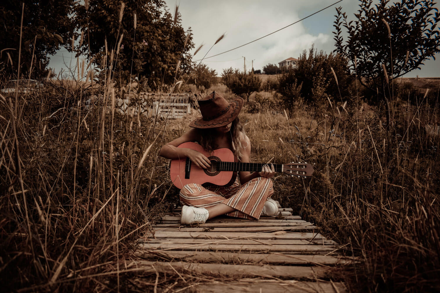 a person with a cowboy hat sitting in the middle of a field holding a guitar 