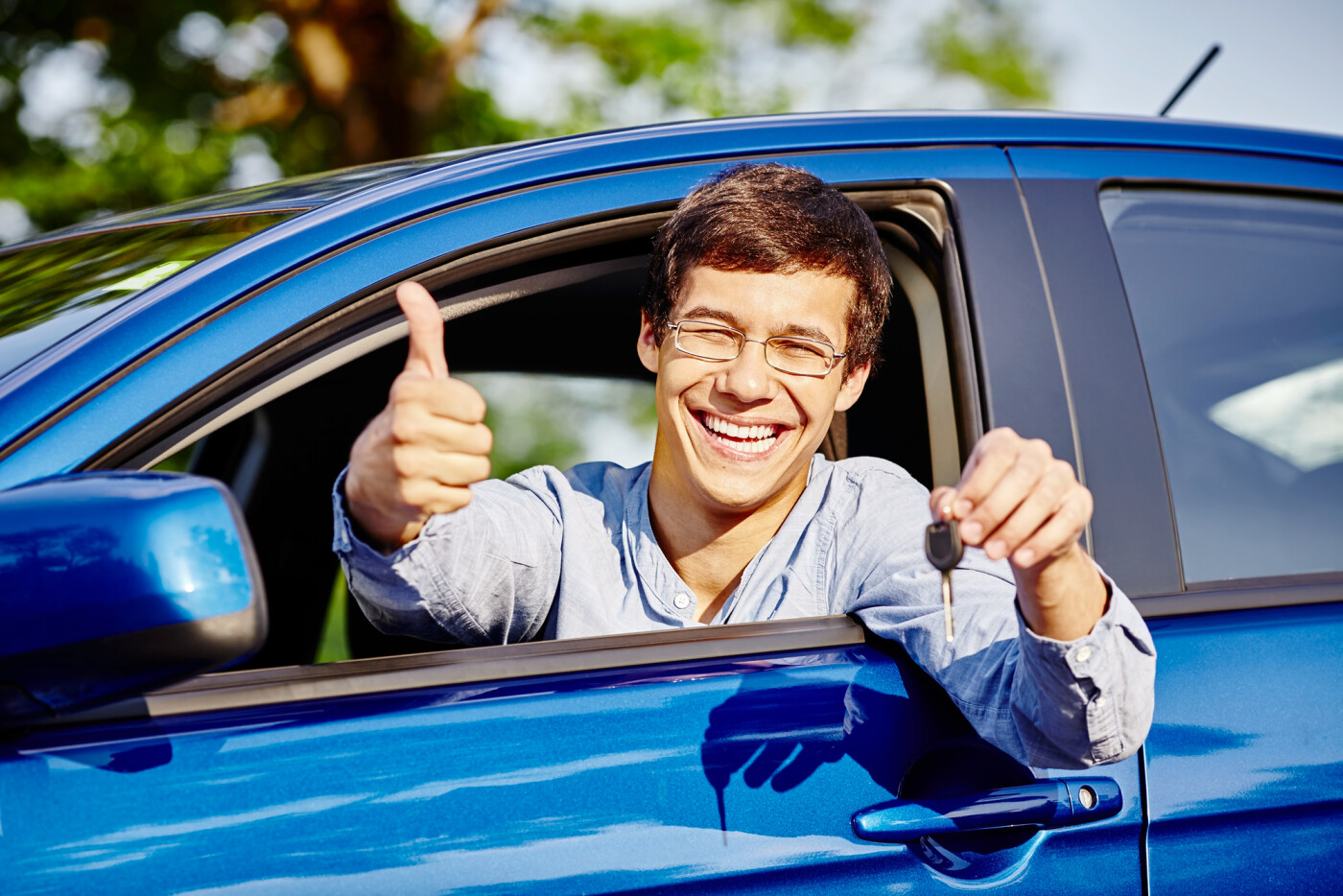 A guy sitting in a car, smiling while showing his car key and giving a thumbs up