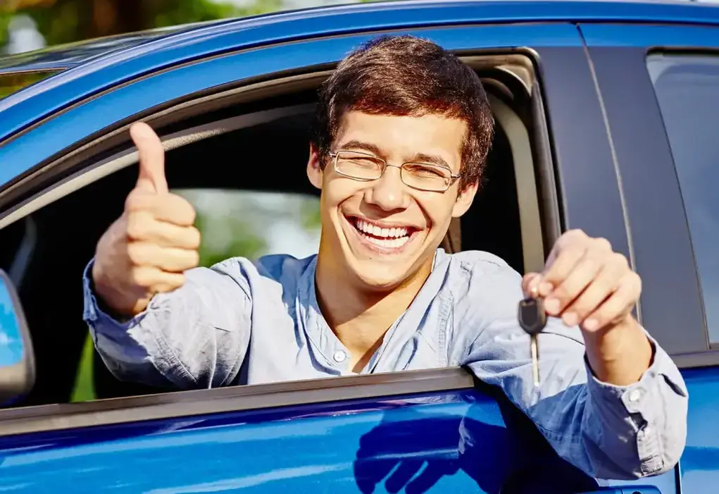 A guy sitting in a car, smiling while showing his car key and giving a thumbs up